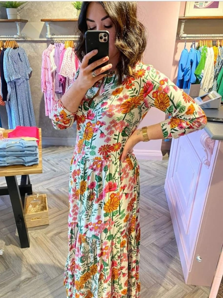 Woman in ireland wearing a maxi length dress with sleeves and tiered skirt and matching gold bracelet and gem ring